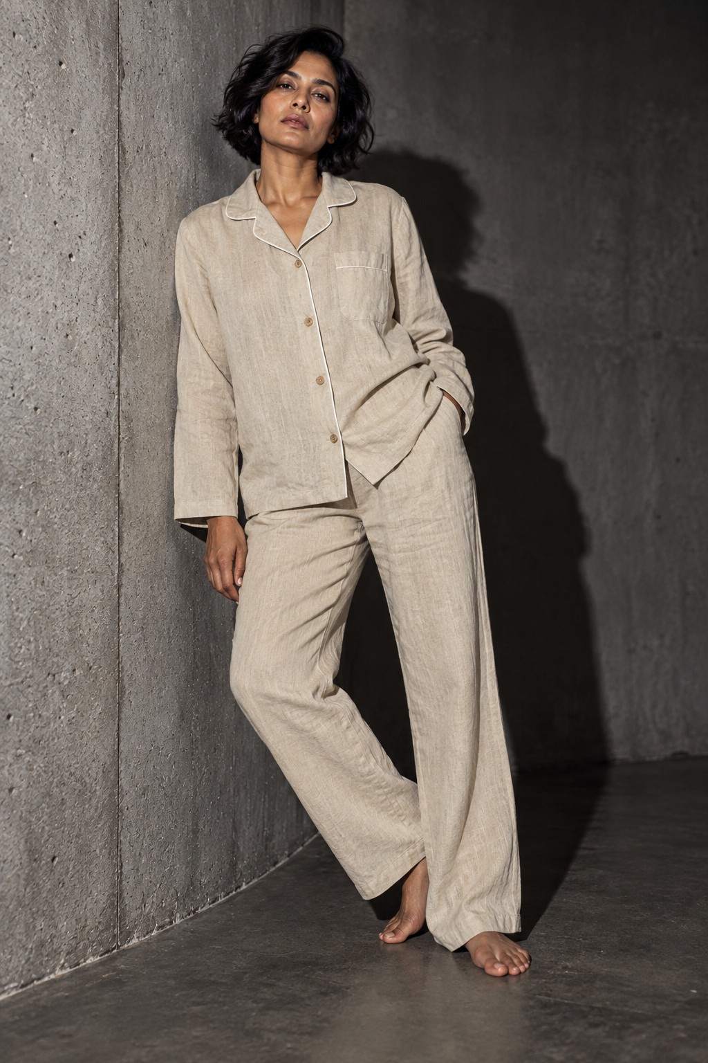 Editorial concept of a curvy woman wearing natural flax-colour linen pyjamas with ivory piping against concrete